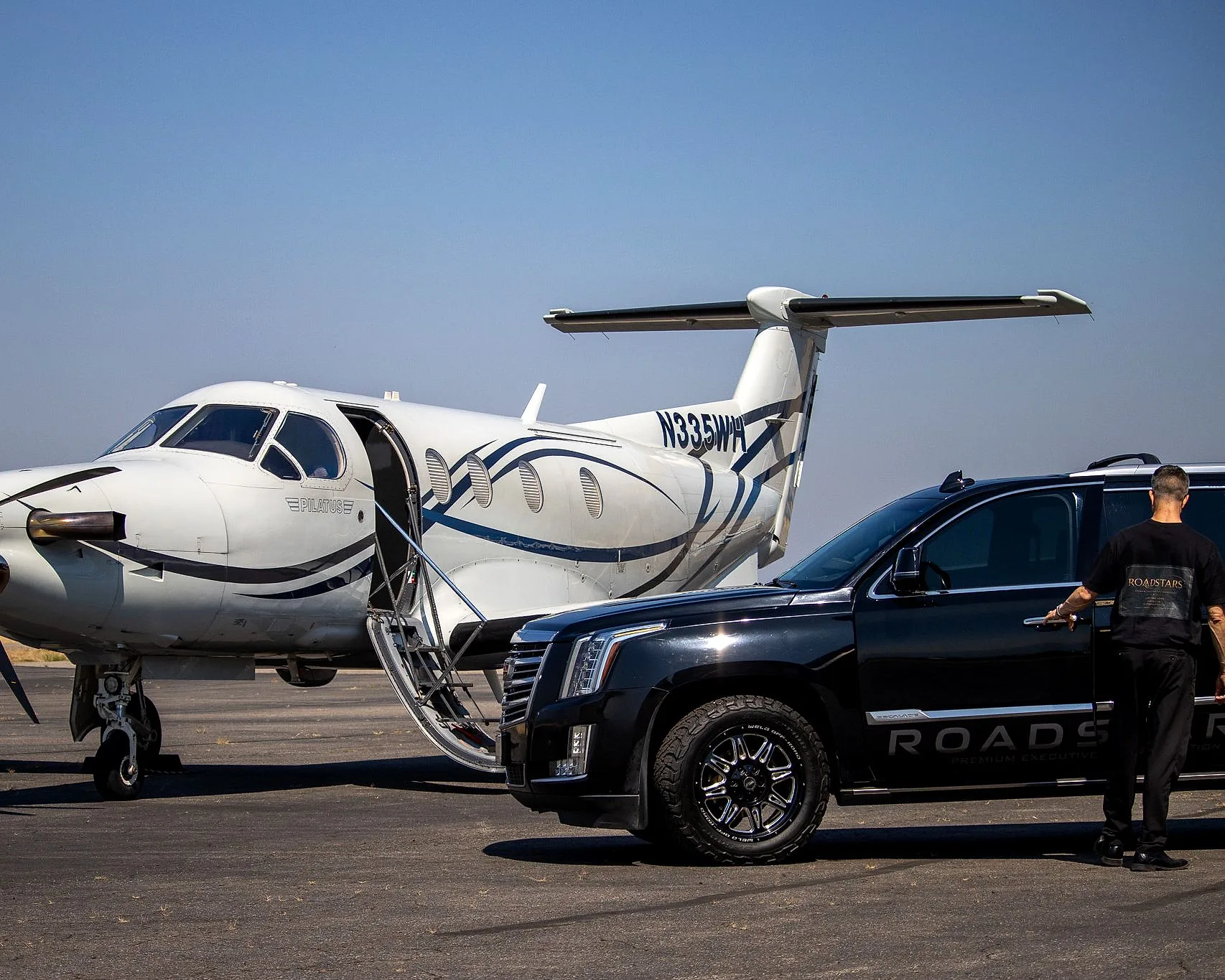 Brandon of RoadStars opening a rear passenger door of the Escalade beside a waiting Pilatus PC-12