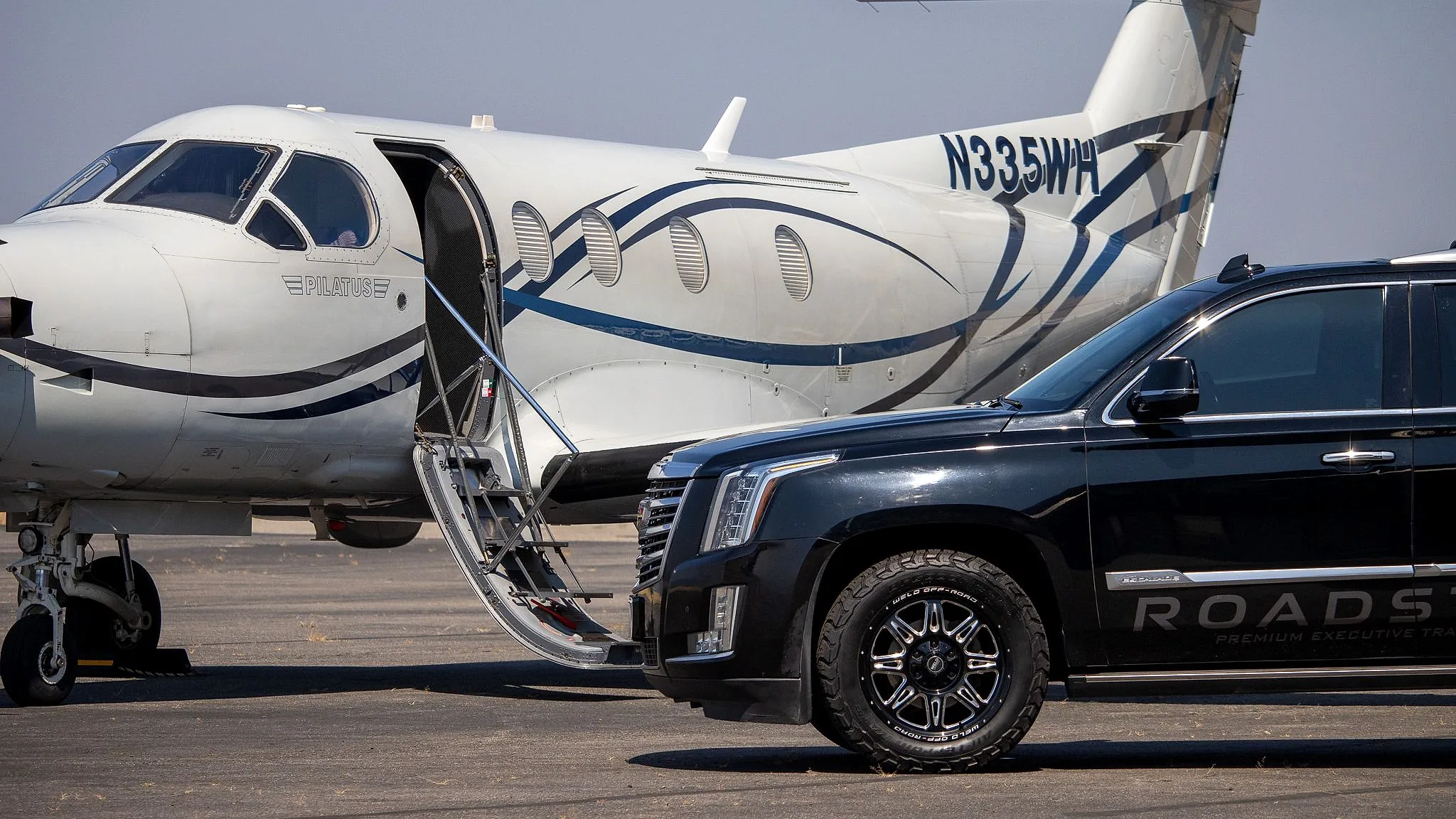 A RoadStars Cadillac Escalade ESV waiting beside a Pilatus PC-12 with its airstair door lowered at Coeur d’Alene Airport