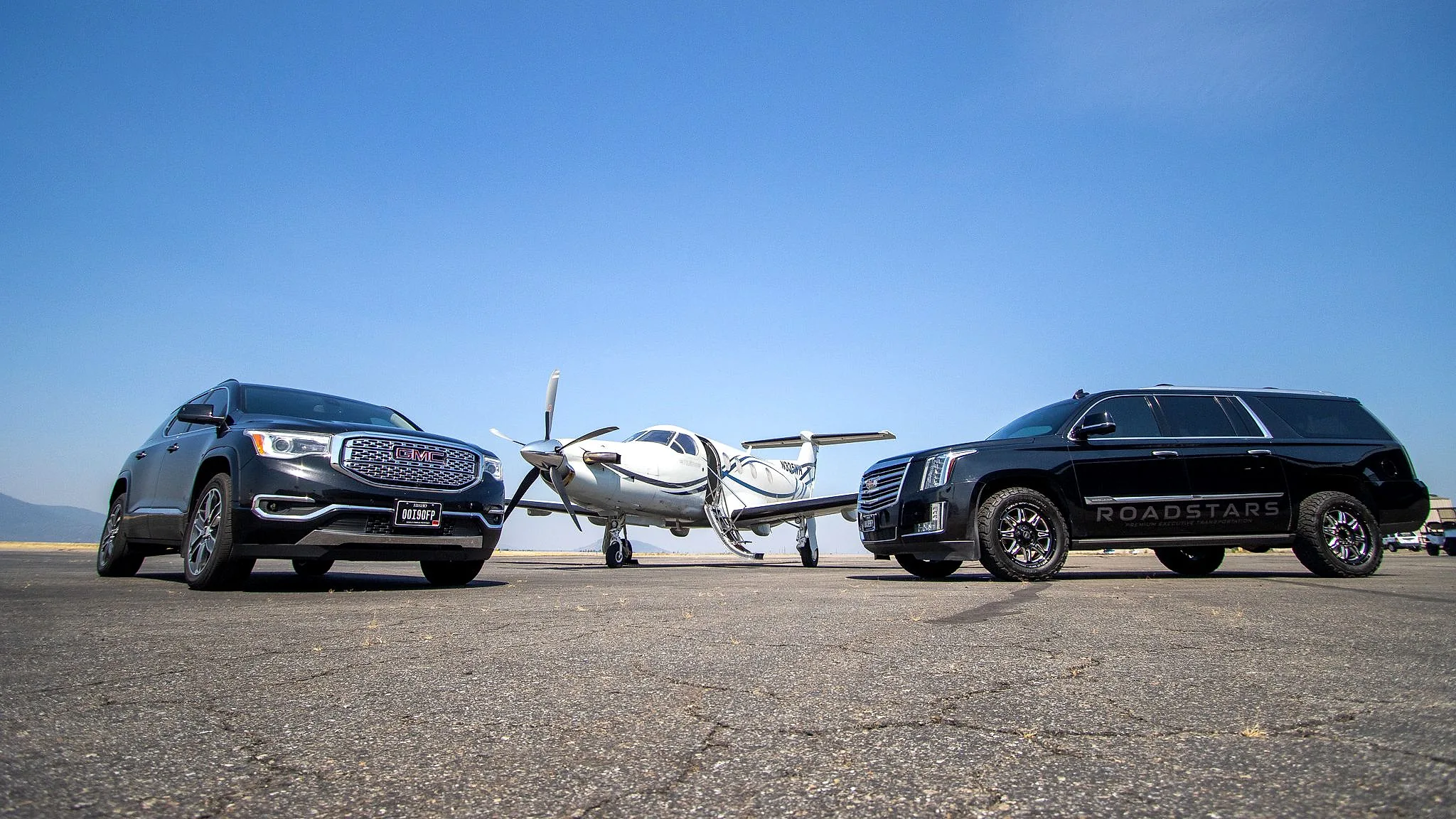 The RoadStars GMC Acadia Denali and Cadillac Escalade ESV parked either side of a private turboprop on the ramp at Coeur d’Alene Airport