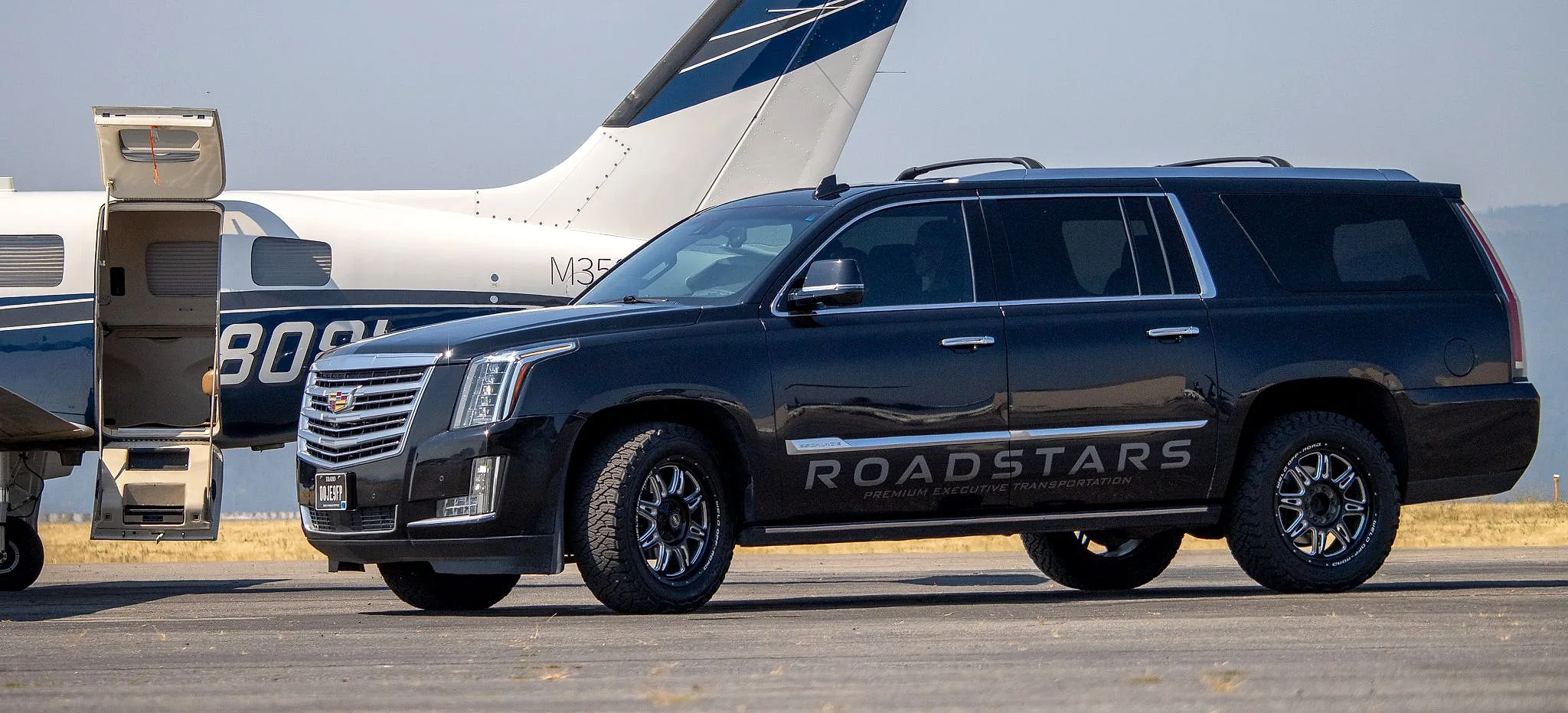 The RoadStars Cadillac Escalade ESV in profile on the ramp, a Piper M350 with its airstair door open behind it
